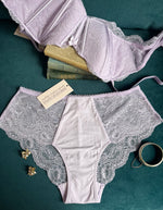 Light Purple Lace Camille Lilac Bralette and matching Lace Camille Lilac Panty lace laid flat. Tag shows Immogene Olivia Gender Euphoric Lingerie. Immogene Olivia Gender euphoric lingerie (bra, bralatte, 40 inch band bra, 42 inch band bra, 44 inch band bra, 46 inch band bra, 48 inch band bra, non  tucking panty, mtf, transgender lingerie, gender inclusive, trans women, trans underwear, gender affirming lingerie)